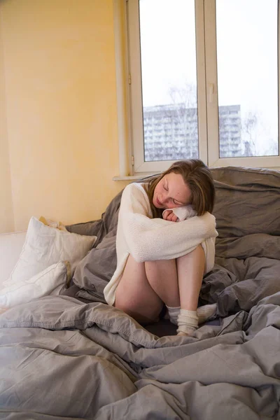 스웨터를 입고 침대에 앉아 무릎을 안고 있는 여자 — 스톡 사진