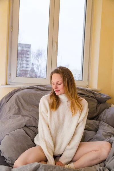 Menina em suéter quente senta-se na posição de lótus na cama — Fotografia de Stock