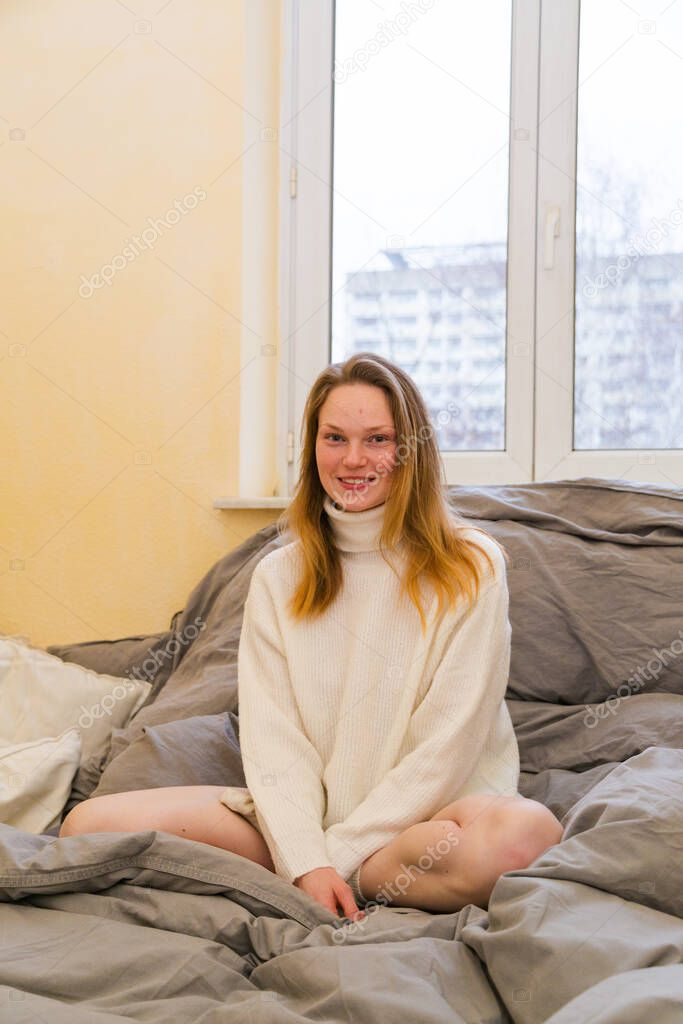 Girl in warm sweater sits in lotus position on bed