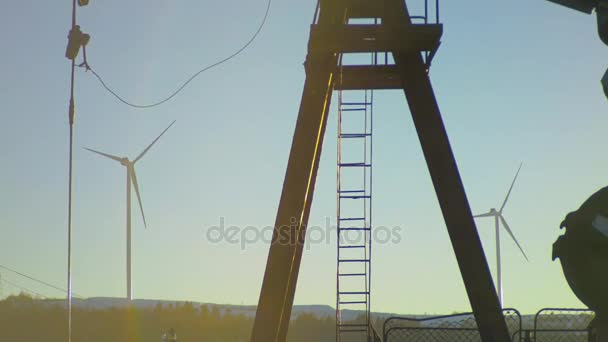 Pumpjack fördert Erdöl auf einer Ölquelle mit Windkraftanlage im Hintergrund — Stockvideo