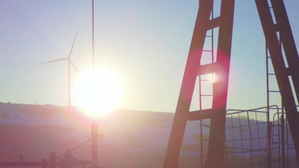 Soleil sur un puits de pétrole avec pompage et centrale éolienne en arrière-plan — Video