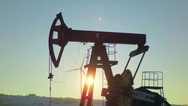 Soleil sur un puits de pétrole avec pompage et centrale éolienne en arrière-plan — Video