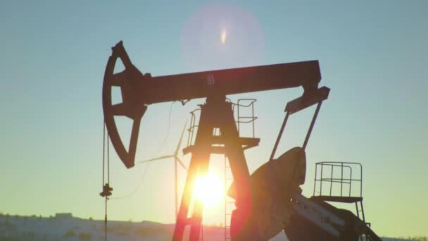 Solsken på en oljekälla med pumpjack och vindkraftverk i bakgrunden — Stockvideo