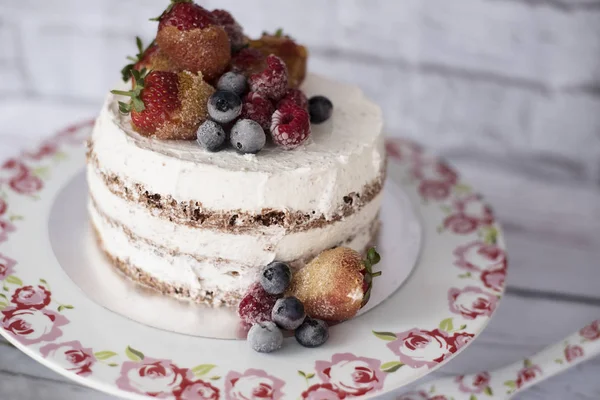 Bolo nu com frutas caramelizadas - morangos, mirtilos, framboesas. Bolo de creme de esponja em planalto alto floral, bandeja. Fundo rústico — Fotografia de Stock