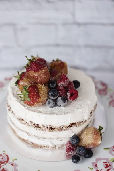 Pastel desnudo con frutas caramelizadas: fresas, arándanos, frambuesas. Pastel de crema de esponja en meseta alta floral, bandeja. Fondo rústico —  Fotos de Stock