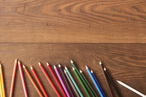 Colorful pencils on the brown wooden table background. Frame of colored pencils over wood with free space for text, copy space