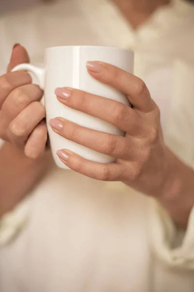 La chica sostiene la taza blanca en las manos. Taza blanca para mujer, regalo. Manos femeninas sosteniendo una taza de café o té caliente por la mañana. Enfoque selectivo —  Fotos de Stock