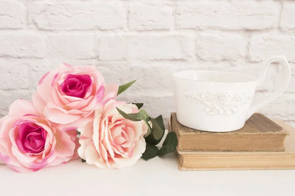 Rosenstrauß auf weißem Schreibtisch, eine große Tasse Kaffee über alten Büchern, romantischer Blumenrahmen, floraler Wandattrappe, Rosenblumen-Attrappe, Valentinstag-Karte, Geschenkkarte — Stockfoto