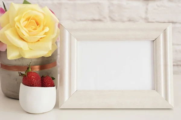 Rahmen-Attrappe. weiße Rahmen-Attrappe auf. Creme Bilderrahmen, Vase mit rosa Rosen, Erdbeeren in Goldschale. Produktrahmen-Attrappe. Wandkunst-Displayvorlage, Ziegelwand — Stockfoto
