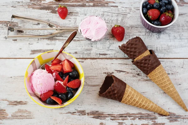 Pink Ice Cream served with berries - strawberries and blueberries in a yellow bowl. Waffle cones with chocolate. Light Rustic Wooden Background — Stock Photo, Image