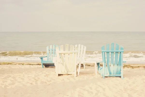 White and blue beach chairs on sand seascape and bright sky in summer vacation relax. Vintage filter tinting, sun haze, glare