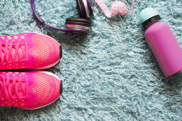 Ζευγάρι ροζ αθλητικά παπούτσια, μετρητής, μπουκάλι νερό και ακουστικών πέρα από γούνα τάπητα. Στο βάθος αίθουσα γυμναστικής. Αξεσουάρ για την εκτέλεση του αθλητισμού και της άσκησης. — Φωτογραφία Αρχείου