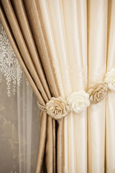 Part of beautifully draped curtain on the window in the room. Floral tieback. Close up of piled curtain. Beige and brown luxury curtain, home interior decor — Stock Photo, Image