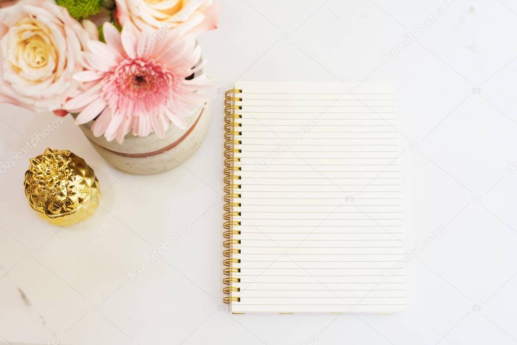 Feminine workplace concept in flat lay style with flowers, golden pineapple, notebook on white marble background. Top view, bright, pink and gold