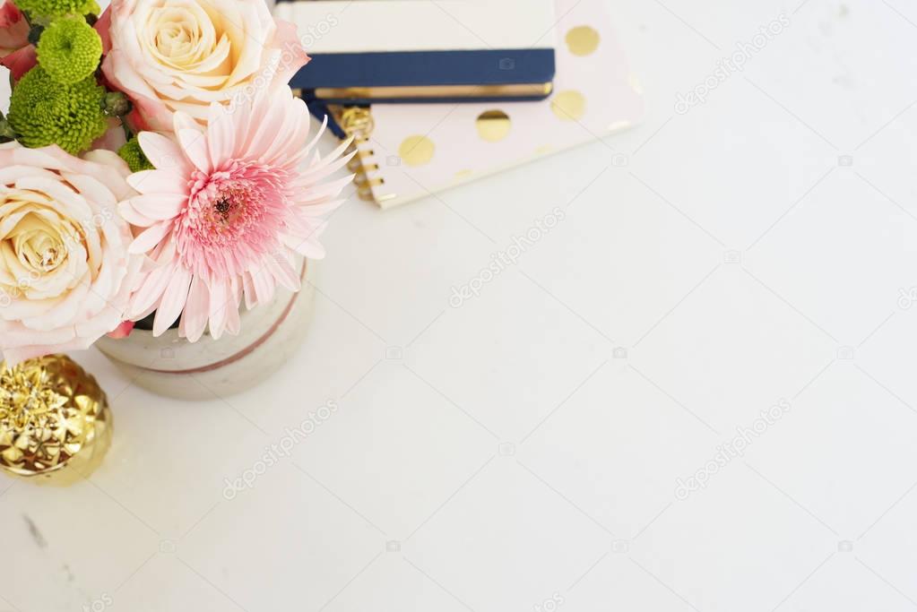 Feminine workplace concept in flat lay style with, flowers, golden pineapple, notebooks on white marble background. Top view, bright, pink and gold