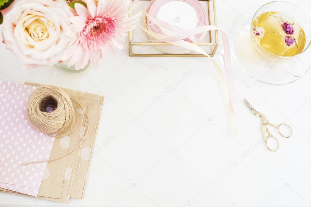 Handmade, craft concept. Handmade goods for packaging - twine, ribbons. Feminine workplace concept. Freelance fashion femininity workspace in flat lay style with flowers, rose tea, notebooks 