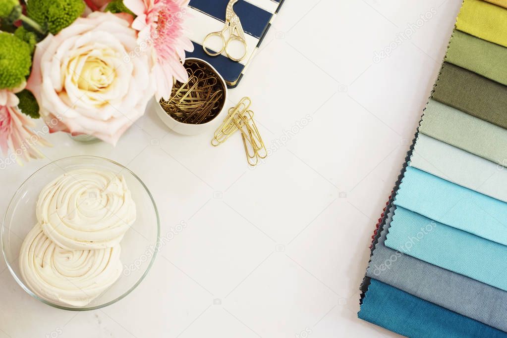 Fabric samples on the table. The designer workplace concept. Freelance fashion comfortable femininity workspace in flat lay style with flowers on white marble background. Top view, bright, pink and go