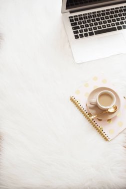 Laptop, kahve ve beyaz kürk halı katta defter. Serbest moda rahat kadınlık ev çalışma alanı düz yatıyordu tarzı. Üstten Görünüm, pembe ve altın. Dikey görüntü, kopya alanı