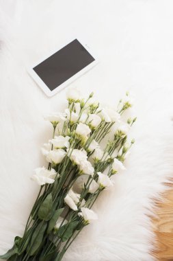Büyük bir buket çiçek ve tablet beyaz kürk Halı zemin üzerinde beyaz. Rahat, moda rahat kadınlık Ev İşyeri. Düz yatıyordu tarzı. Üstten Görünüm, dikey görüntü