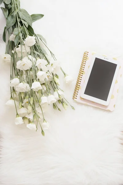 Cuaderno, tableta y un gran ramo de flores blancas en el suelo sobre una alfombra de piel blanca. Moda independiente feminidad cómoda espacio de trabajo en casa en estilo plano laico. Vista superior, rosa y oro. Imag vertical —  Fotos de Stock