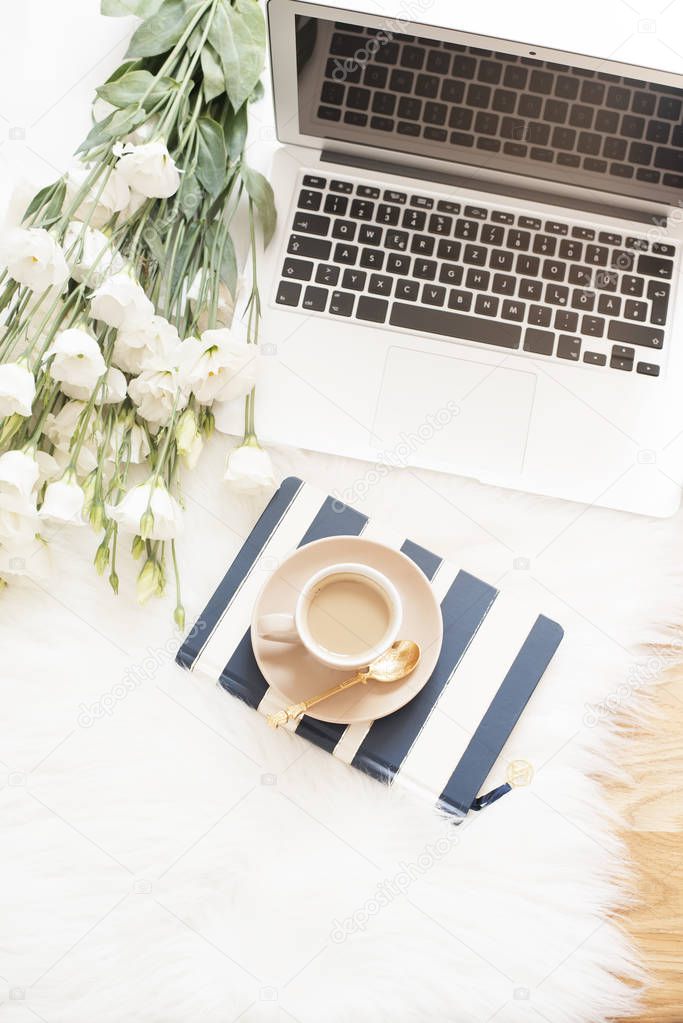 Notebook, laptop, a cup of coffee and a large bouquet white flowers on the floor on a white fur carpet. Freelance fashion comfortable femininity home workspace in flat lay style. Top view, stripe and 