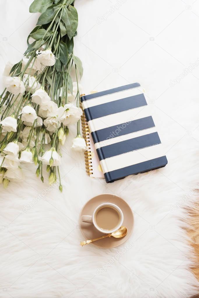 Notebook, tablet, a cup of coffee and a large bouquet white flowers on the floor on a white fur carpet. Freelance fashion comfortable femininity home workspace in flat lay style. Top view, stripe and 