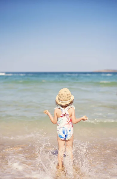Niña, niña con sombrero de paja y traje de baño floral mirando al mar en un día soleado — Foto de Stock