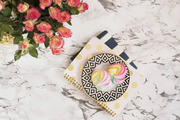Feminine workplace concept. Freelance workspace in flat lay style with sweets, flowers, notebooks on white marble background. Top view, bright, pink, stripe and gold