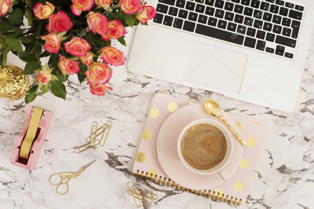 Feminine workplace concept. Freelance workspace in flat lay style with laptop, coffee, flowers, golden pineapple, notebook and paper clips on white marble background. Top view, bright, pink and gold