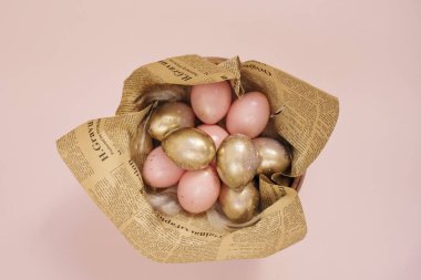Ahşap bir kasede yumurta. Pembe ve altın yumurta. Pembe Pastel Paskalya yumurta ve tüyleri ve Vintage gazete konseptiyle