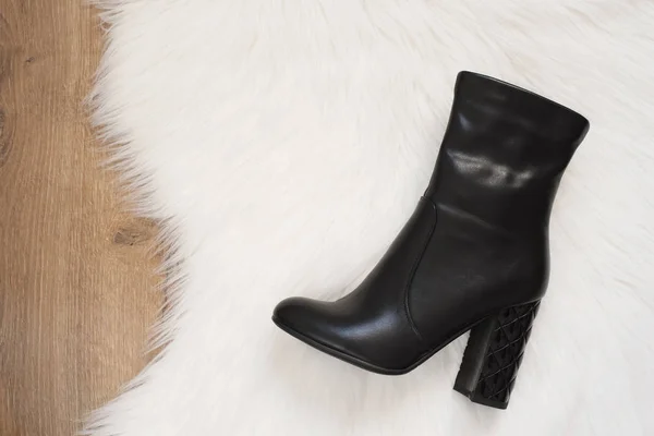 Κομψές γυναίκες μαύρο ψηλές μπότες τακούνια. Κάτοψη της μαύρες μπότες σε ένα χαλί λευκή γούνα, ξύλινο υπόβαθρο. Έννοια της μόδας και του design, ψώνια — Φωτογραφία Αρχείου