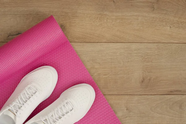 Rosa yogamatta och vita trendiga sneakers på en trä bakgrund. Fitness-konceptet, aktiv livsstil, kropp vård koncept. Trä bakgrund — Stockfoto