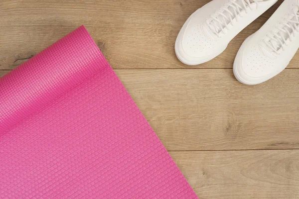 Rosa yogamatta och vita trendiga sneakers på en trä bakgrund. Fitness-konceptet, aktiv livsstil, kropp vård koncept. Trä bakgrund — Stockfoto