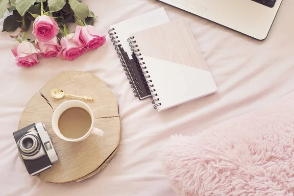 Kaffee, alte Vintage-Kamera im Bett auf rosa Laken. Rosen, Notebooks und Laptops liegen herum. freischaffender Mode-Home-Weiblichkeit-Arbeitsplatz im flachen Lay-Stil — Stockfoto