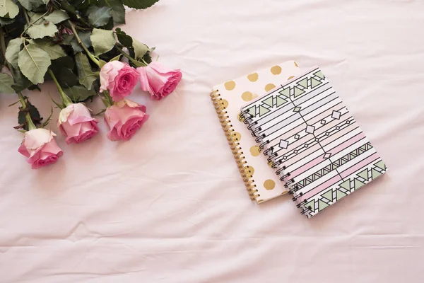 Bingkai bunga dengan mawar merah muda yang menakjubkan dan buku catatan pada seprai merah muda di kamar tidur. Ruang kerja lepas. Pernikahan, kartu hadiah, hari kasih sayang atau latar belakang hari ibu — Stok Foto