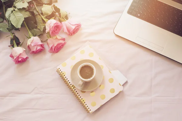 Kaffee, alte Vintage-Kamera im Bett auf rosa Laken. Rosen, Notebooks und Laptops liegen herum. freischaffende Mode zu Hause Weiblichkeit Arbeitsbereich — Stockfoto