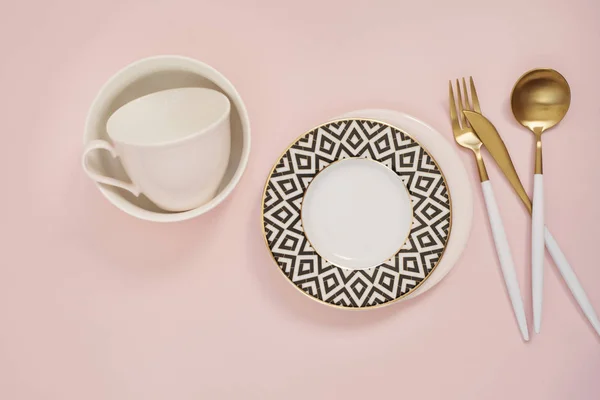 Goldbesteck vorhanden. goldenes Löffelset, goldenes Messer, Löffel, Gabel, Kaffeetasse und leeres Geschirr auf dem Tisch. Luxus-Kochlöffel von oben. Pastellrosa Hintergrund — Stockfoto