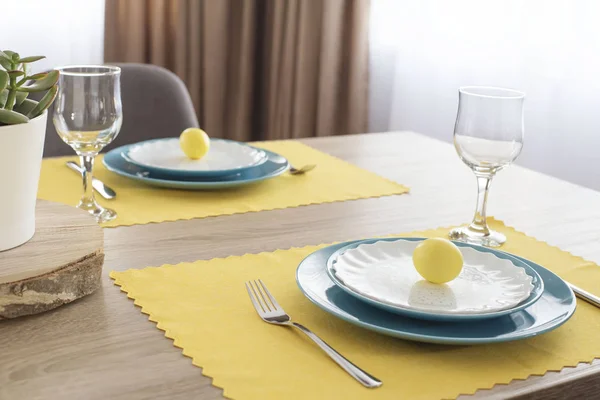 Hermoso ajuste de mesa de Pascua con decoraciones. Placas azules en alfombras de alimentación amarillas. Huevos pintados de Pascua amarillos —  Fotos de Stock