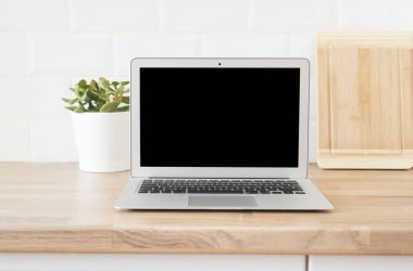 İçişleri Bakanlığı. Evden çalışmak. Modern bilgisayar, boş ekranlı dizüstü bilgisayar. Parlak ve Temiz Modern Minimalist Mutfak, Yakın çekim. Tahta kesme tahtaları, ahşap atölyedeki yeşil sulu tencere..