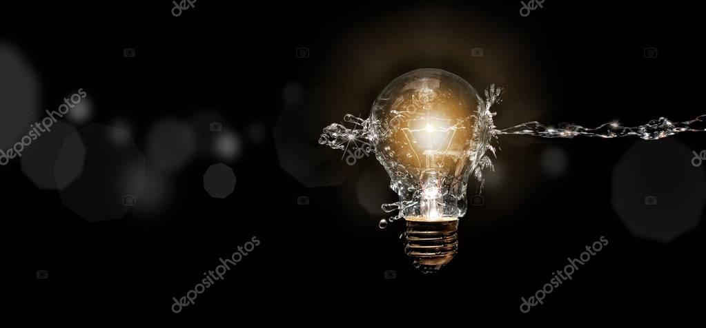 Spray of water against light bulb on black background