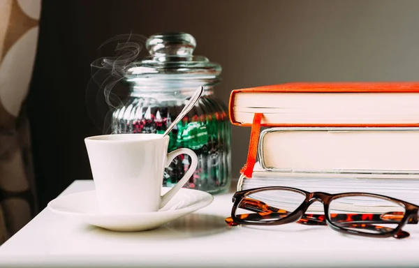 Cup of coffee on the table with books and reading glasses