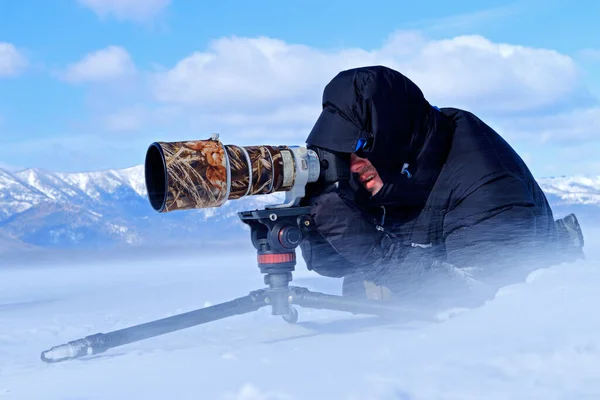 Winter photography, man in the snow with camera. Snow lake with ice in Japan. Whooper Swans, Cygnus cygnus, birds in the nature habitat, Lake Kusharo, winter scene with snow , Hokkaido, Japan.