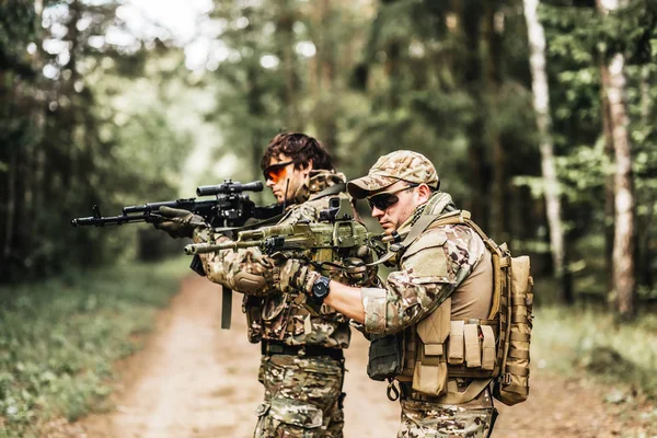 Dois militares homens armados em uma zona de soldado de conflito armado em uniforme visando com espingarda de assalto ao ar livre. duas soldas com arma — Fotografia de Stock