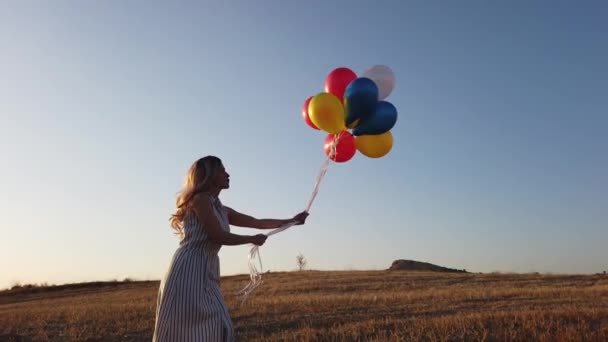 夏には自然に夕日を眺めながら草原を駆け抜ける風船を持つ幸せな陽気な女の子 ドローンビュー4K — ストック動画