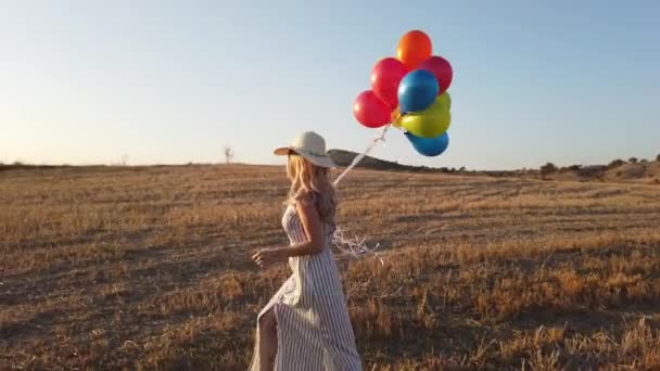夏には自然に夕日を眺めながら草原を駆け抜ける風船を持つ幸せな陽気な女の子 ドローンビュー4K — ストック動画