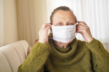 Corona virüsüne karşı korunmak için cerrahi maske takan yaşlı kadının portresi. Büyükannem oturma odasında oturuyor ve yukarı bakıyor. 
