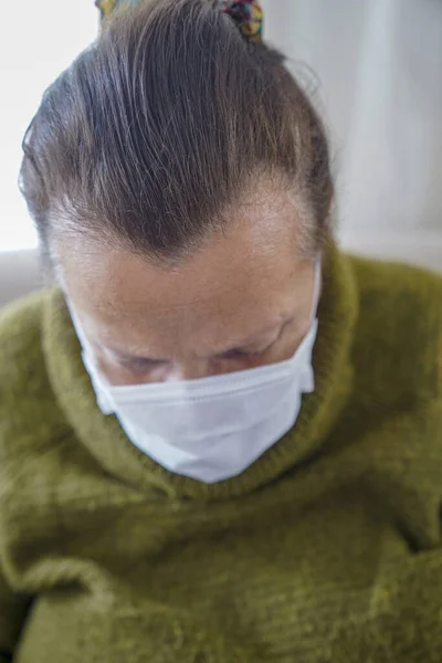 コロナウイルスに対する保護のために外科用マスクを身に着けている老婦人の肖像 祖母は彼女のリビングルームに座って検索します — ストック写真