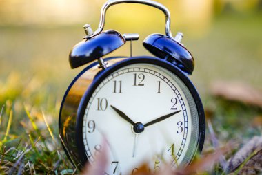 Bahar Zamanı Değişimi 'nin resmi. Yaz dönemi konsepti. Dışarıda klasik çalar saat var. Yeşil çimenlerdeki çalar saat