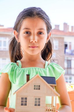 Küçük kız ahşap ev modelini tutuyor. Hortum, ipotek, aile ve finansal konsept. Resim
