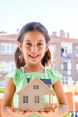 Küçük kız ahşap ev modelini tutuyor. Hortum, ipotek, aile ve finansal konsept. Resim